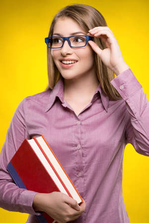 Intelligence female student. Smiling young women holding books in her hand while standing against yellow backgroundの写真素材