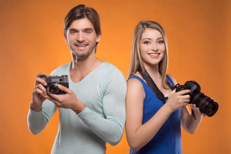 Photographers. Two cheerful photographers holding cameras in their hands and smiling while isolated on coloured backgroundの写真素材