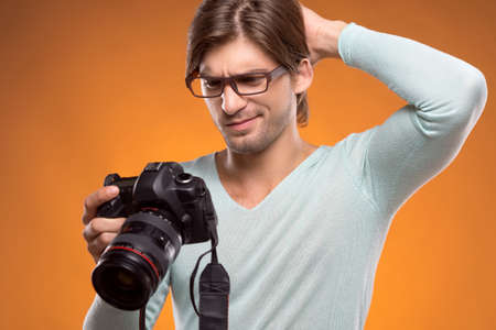 Man with camera. Frustrated young man holding camera in his hands and looking at it while isolated on greyの写真素材