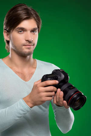 Man with camera. Confidenct young man holding camera in his hands and looking at you while isolated on greenの写真素材