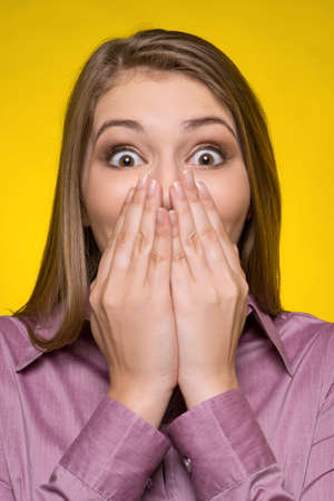 Shocked woman. Surprised young woman covering mouth with hands and looking at camera while isolated on yellowの写真素材