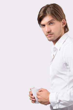 Man with cup. Portrait of pensive young man holding cup and looking at camera while isolated on whiteの写真素材