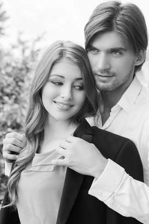 Beautiful couple. Black and white image of beautiful young couple standing close to each other while man covering woman with his suitの写真素材
