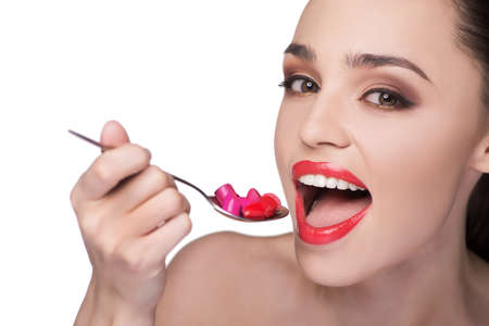 Beautiful women holding a spoon with multi colored lipsticks on it while isolated on white