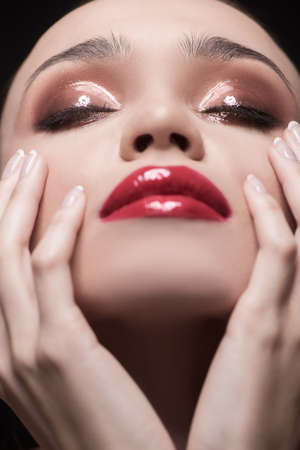 Portrait of beautiful women touching face with both hands and keeping eyes closed while isolated on blackの写真素材