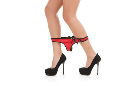 Red panties. Cropped image of young women in high heeled shoes taking down her red panties while standing isolated on whiteの写真素材