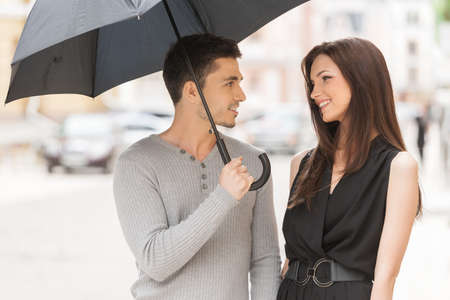 Loving couple. Cheerful young couple standing close to each other while man holding umbrellaの写真素材