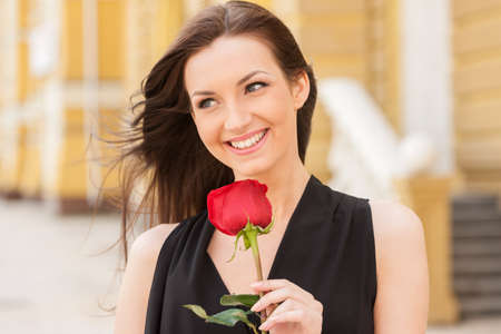 Girl with flower. Beautiful young woman holding red rose and smilingの写真素材