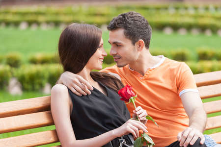 Loving couple on the bench. Beautiful young couple sitting close to each other on the bench and looking at each otherの写真素材