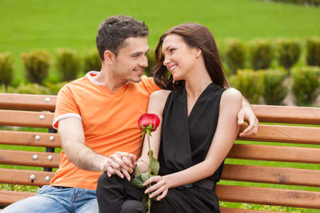 Loving couple on the bench. Cheerful young couple sitting close to each other on the bench and looking at each otherの写真素材