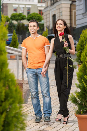 Happy loving couple. Full length of cheerful young couple holding hands and looking awayの写真素材