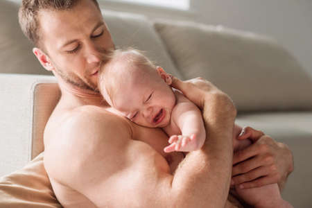 Man with baby. Young muscular man holding a crying baby in his handsの写真素材