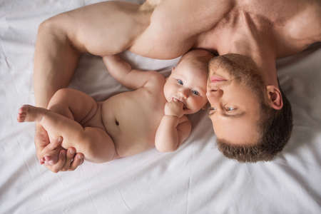 Man with little baby. Top view of young muscular man and little baby lying close to each otherの写真素材