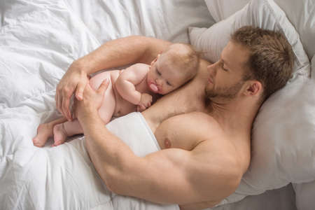 Man with little baby. Young muscular man and little baby lying on the bedの写真素材
