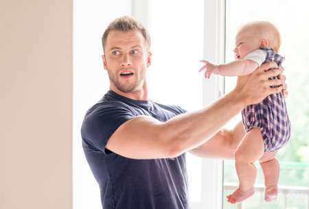 Man with baby. Frustrated young man holding baby in his hands and looking awayの写真素材