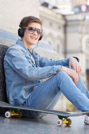 Teenager. Cheerful teenager sitting near his skate and smiling at cameraの写真素材