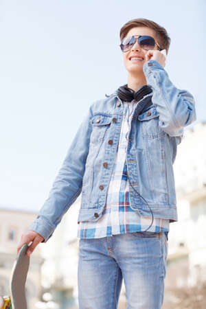 Teenager. Low angle view of cheerful teenager holding skate and talking on the phoneの写真素材