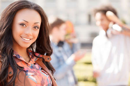 Teenage friends. Cheerful teenage girl smiling at camera while her friends talking on the backgroundの写真素材