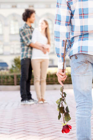 Broken heart. Cropped image of man holding red rose while couple hugging on the backgroundの写真素材