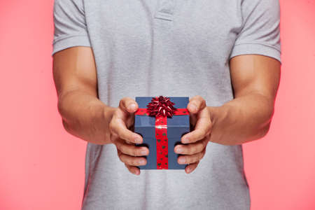 Gift box. Cropped image of man holding a gift box while standing against red backgroundの写真素材