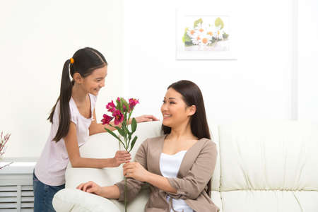 Mother and daughter. Cheerful daughter presenting flowers to motherの写真素材