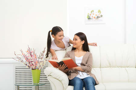 Mother and daughter. Cheerful daughter and mother reading book togetherの写真素材