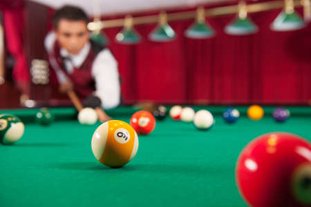 Playing pool. Confident young man aiming the billiard ball with cueの写真素材