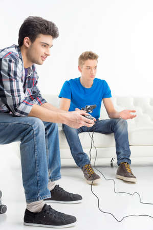 Two young gamers playing video games while sitting on the couch isolated on whiteの写真素材