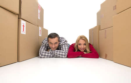 Happy couple. Cheerful middle-aged couple lying together between two cardboard box stacks and smilingの写真素材