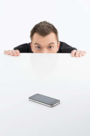 Scared businessman. Terrified young men looking out of the table with mobile phone on itの写真素材