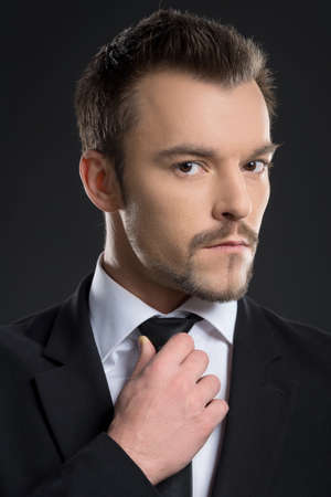 Bossy men. Bossy young men adjusting his necktie while standing isolated on blackの写真素材