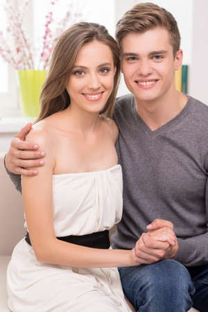 Loving couple at home. Beautiful young couple hugging and smiling while sitting on the couchの写真素材