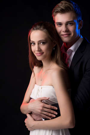 Loving couple. Beautiful young couple in formalwear hugging and smiling at cameraの写真素材