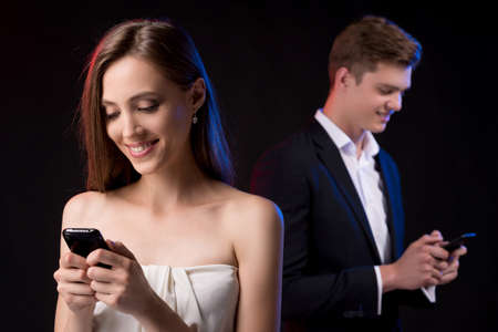 Staying connected. Beautiful young couple holding mobile phones in hands and smilingの写真素材