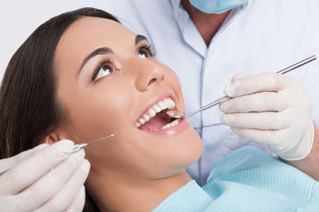 Patient at dentist office. Close-up of young woman sitting at the chair in dental office and doctor examining teethの写真素材