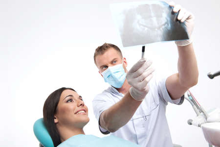 Patient at dentist office. Beautiful young woman sitting at the chair in dental office while doctor showing something at X-ray photoの写真素材