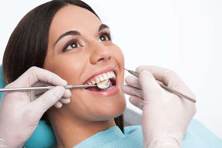 Patient at dentist office. Close-up of cheerful young woman sitting at the chair in dental office and doctor examining teethの写真素材