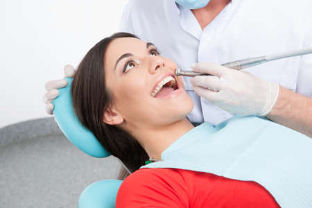 Patient at dentist office. Top view of beautiful young woman sitting at the chair in dental office and doctor examining teethの写真素材