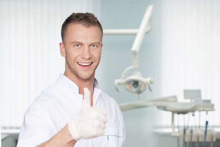 Cheerful dentist. Smiling young dentist in protective gloves looking at camera and gesturingの写真素材