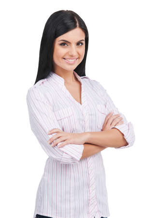 Confident woman. Cheerful young woman keeping arms crossed and smiling while standing isolated on whiteの写真素材