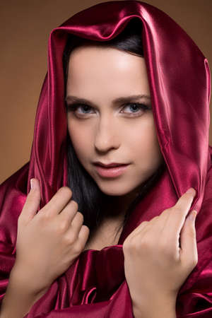 Mysterious look. Attractive young woman covered with red cloth looking at cameraの写真素材