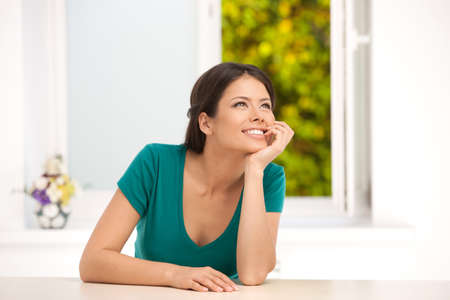 Girl dreaming  Beautiful young woman sitting at the table and holding hand on chinの写真素材
