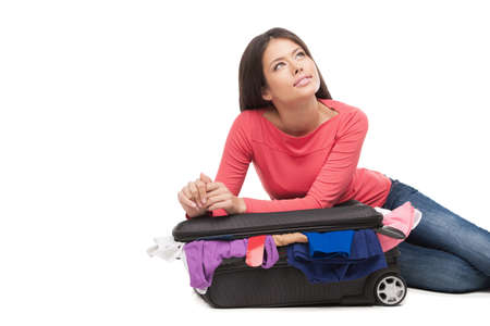 Girl dreaming. Beautiful young woman sitting near the suitcase and looking away while isolated on whiteの写真素材