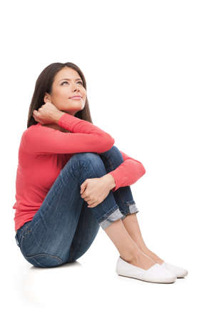 Girl dreaming. Beautiful young woman sitting on the floor and looking away while isolated on whiteの写真素材