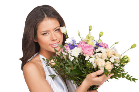 Girl with flowers. Cheerful young woman in white holding bunch on flowers and smiling while standing isolated on whiteの写真素材