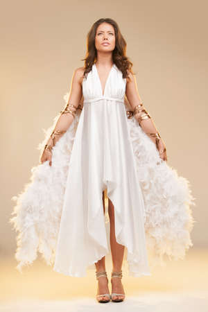 Girl with wings. Full length of beautiful young woman with white wings looking away while standing isolated on colored backgroundの写真素材