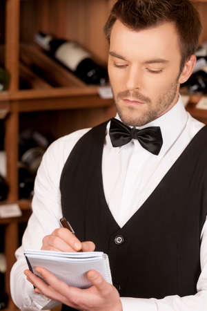 Confident sommelier. Thoughtful young sommelier writing something ay his note padの写真素材