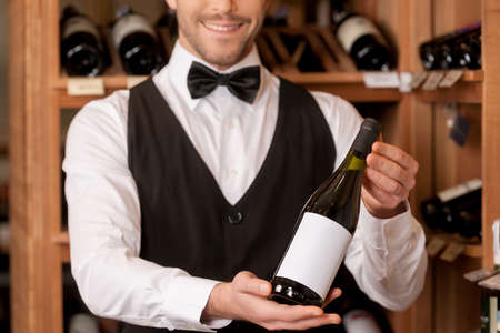 Confident sommelier. Cropped image of cheerful young sommelier holding a wine bottle and smilingの写真素材