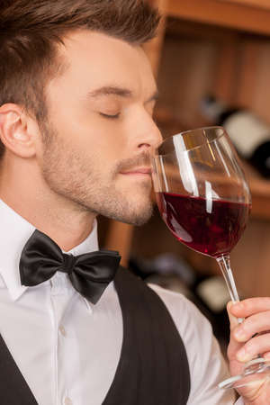 Confident sommelier. Side view of confident young sommelier holding a wine glass and keeping his eyes closedの写真素材