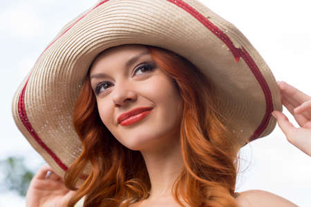 Red hair beauty. Portrait of beautiful young red hair woman in hat smiling and looking awayの写真素材